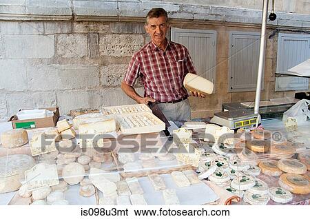 Stock Photograph - Man at sheeps cheese market stall in france. Fotosearch