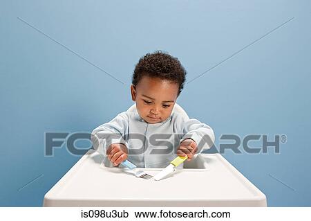 Baby boy sitting in highchair using knife and fork View Large Photo Image Stock Image - Baby boy sitting in highchair using knife and fork. Fotosearch