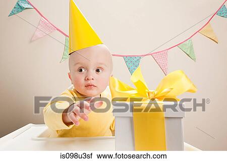 Stock Image - Baby boy sitting in highchair with gift box. Fotosearch