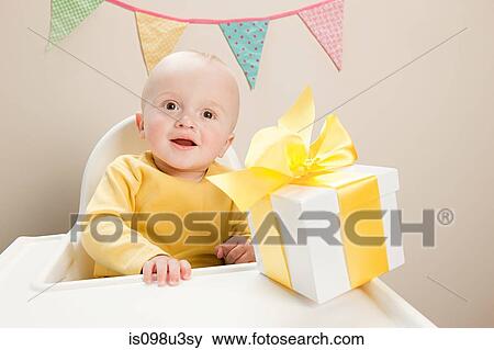 Stock Photo - Baby boy sitting in highchair with gift box. Fotosearch
