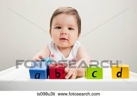Stock Image - Baby boy sitting in highchair with wooden alphabet blocks. Fotosearch
