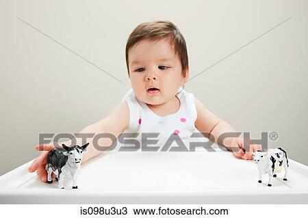 Stock Image - Baby boy sitting in highchair with toy cows. Fotosearch