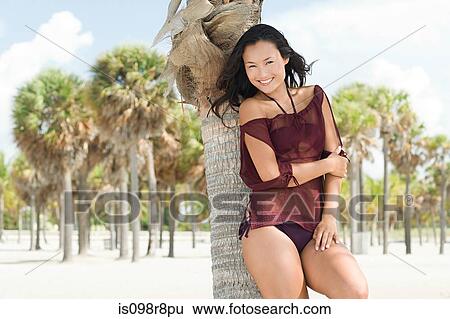 Young woman on beach by palm tree View Large Photo Image Stock Photograph - Young woman on beach by palm tree. Fotosearch