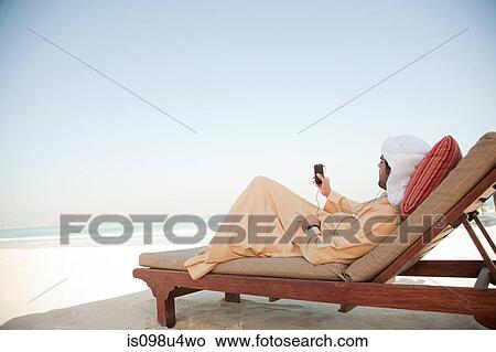 Picture - Middle Eastern man listening to music on mobile phone. Fotosearch