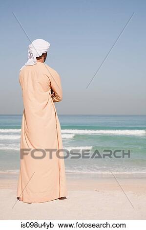 Stock Image - Middle Eastern man standing on the beach. Fotosearch