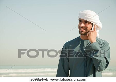 Middle Eastern man using mobile phone on the beach View Large Photo Image Stock Image - Middle Eastern man using mobile phone on the beach. Fotosearch