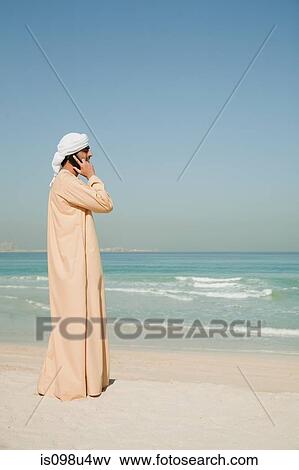 Middle Eastern man using mobile phone on the beach View Large Photo Image Stock Photo - Middle Eastern man using mobile phone on the beach. Fotosearch