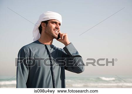 Stock Photo - Middle Eastern man using mobile phone on the beach. Fotosearch
