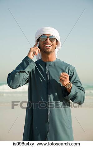 Stock Photo - Middle Eastern man using mobile phone on the beach. Fotosearch