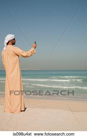 Middle Eastern man using mobile phone on the beach View Large Photo Image Stock Photograph - Middle Eastern man using mobile phone on the beach. Fotosearch