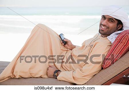 Stock Image - Middle Eastern man with mobile phone on sun lounger. Fotosearch