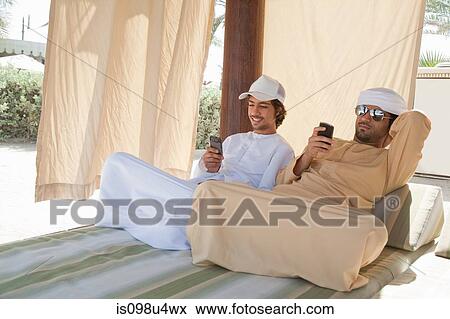 Stock Photo - Two Middle Eastern men sitting on bed. Fotosearch