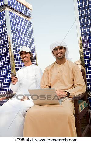 Stock Image - Two Middle Eastern men with laptop and mobile phone. Fotosearch
