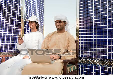 Stock Photograph - Two Middle Eastern men with laptop and mobile phone. Fotosearch