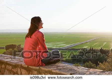 Young woman sitting on stone wall View Large Photo Image Stock Image - Young woman sitting on stone wall. Fotosearch