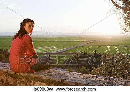 Stock Photograph - Young woman sitting on stone wall. Fotosearch