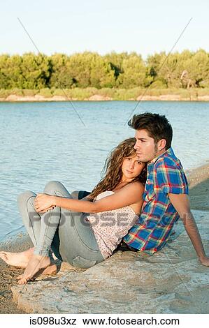 Stock Photo - Young couple sitting near lake. Fotosearch