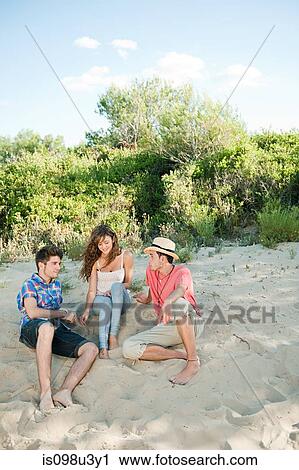 Young friends sitting on sand View Large Photo Image Stock Image - Young friends sitting on sand. Fotosearch