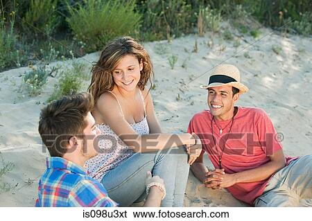Young friends sitting on sand View Large Photo Image Stock Photograph - Young friends sitting on sand. Fotosearch
