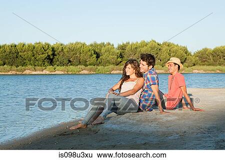 Young friends sitting on sand View Large Photo Image Stock Photograph - Young friends sitting on sand. Fotosearch