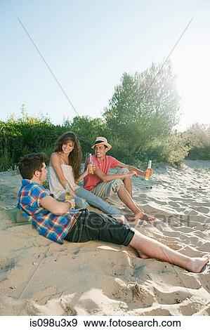 Young friends sitting on sand with beer View Large Photo Image Stock Photo - Young friends sitting on sand with beer. Fotosearch