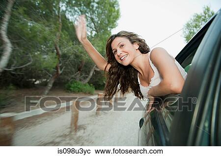 Stock Image - Young woman waving from car window. Fotosearch