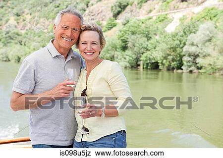 Stock Photo - Senior couple with glasses of wine on a boat holiday. Fotosearch