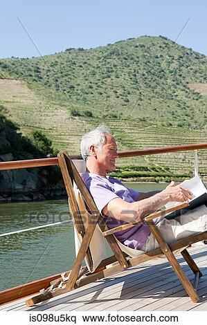 Stock Photography - Senior man reading book on a boat holiday. Fotosearch
