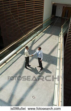 Businessmen shaking hands on office walkway View Large Photo Image Stock Image - Businessmen shaking hands on office walkway. Fotosearch