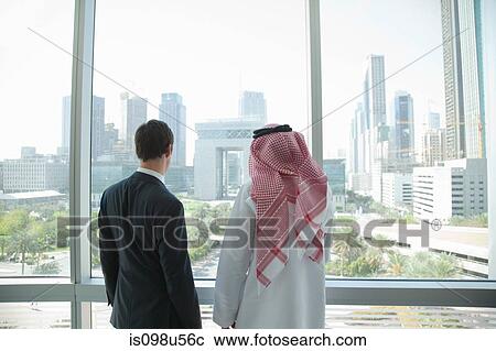 Stock Image - Western and middle eastern businessmen by window of dubai office. Fotosearch