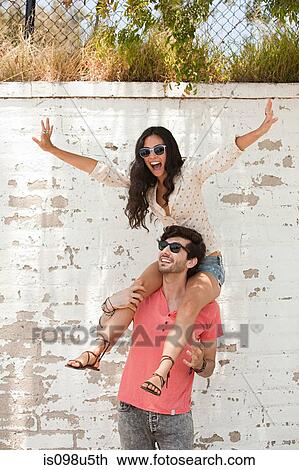 Stock Image - Young man with young woman on shoulders. Fotosearch