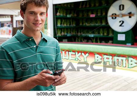 Teenage boy using cellphone at fun fair View Large Photo Image Stock Image - Teenage boy using cellphone at fun fair. Fotosearch