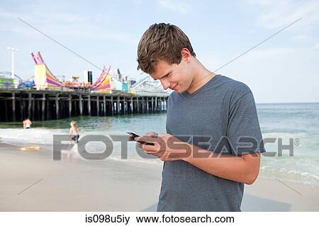 Teenage boy using cellphone on beach View Large Photo Image Stock Photo - Teenage boy using cellphone on beach. Fotosearch
