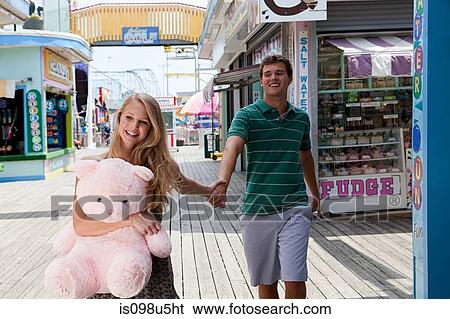 Teenage couple holding hands on boardwalk with teddy bear View Large Photo Image Stock Photograph - Teenage couple holding hands on boardwalk with teddy bear. Fotosearch