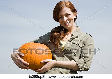 Stock Image - Young woman holding a pumpkin. Fotosearch