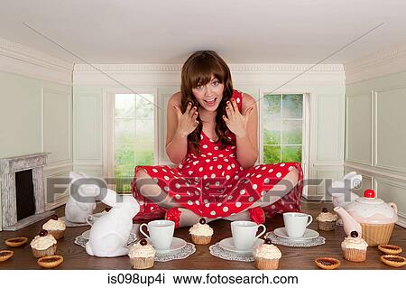 Stock Image - Young woman having tea party in small room. Fotosearch