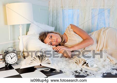 Stock Image - Young woman lying amongst pillow feathers in small room. Fotosearch