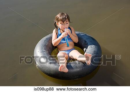 Stock Photo - Girl eating lolly on inflatable ring in lake. Fotosearch