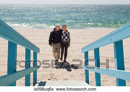 Stock Photo - Couple walking on beach towards walkway. Fotosearch