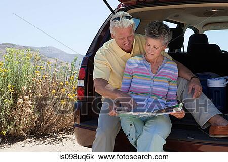 Stock Image - Mature couple sitting on boot of car with map. Fotosearch