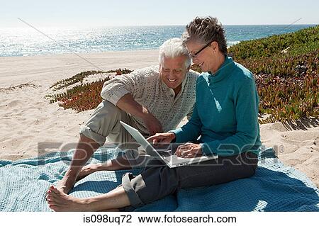 Mature couple using laptop at the beach View Large Photo Image Stock Image - Mature couple using laptop at the beach. Fotosearch