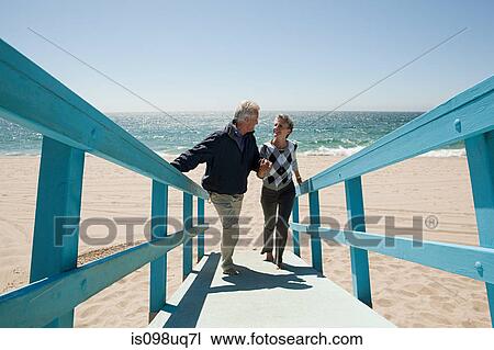 Stock Image - Mature couple walking on beach walkway. Fotosearch