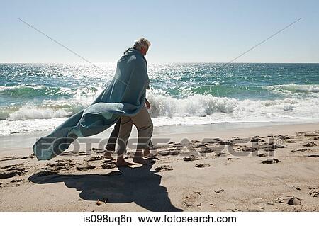 Mature couple walking on beach wrapped in blanket View Large Photo Image Picture - Mature couple walking on beach wrapped in blanket. Fotosearch