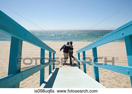 Stock Photograph - Rear view of couple on beach walkway. Fotosearch
