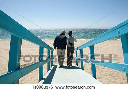 Stock Photograph - Rear view of couple on beach walkway. Fotosearch