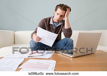 Worried young man with paperwork using laptop View Large Photo Image Stock Image - Worried young man with paperwork using laptop. Fotosearch