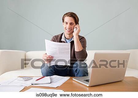 Stock Image - Young man with paperwork using laptop. Fotosearch