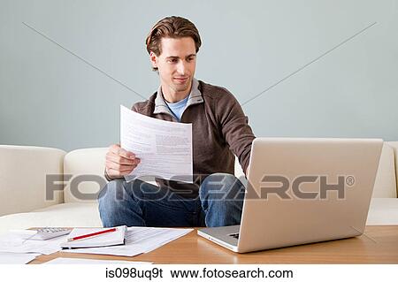 Stock Photograph - Young man with paperwork using laptop. Fotosearch