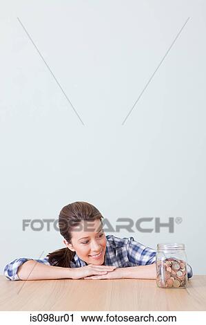 Stock Image - Young woman with jar of coins. Fotosearch