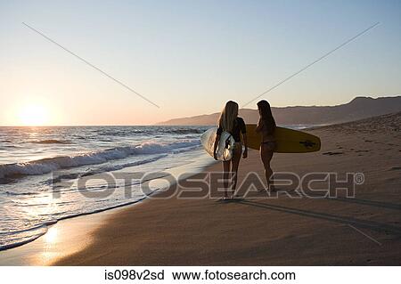 Stock Image - Female surfers by the sea at sunset. Fotosearch